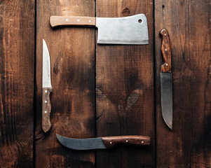 set of different kitchen knives with wooden handles on a brown background from boards, top view