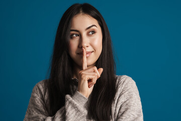 Pleased beautiful asian girl smiling and showing silence gesture