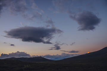 Atmospheric minimal mountain scenery with lilac dawn sky. Scenic minimalist landscape with purple sunset in mountains. Beautiful sunrise in mountains in pastel tones. Rocky mountain in dawn cloudy sky