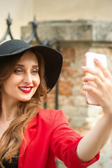 Beautiful smiling caucasian young woman taking selfie on the smartphone against an urban background