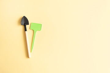 Miniature gardening tools and inscription board on beige background.