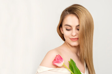 Obraz na płótnie Canvas Beautiful caucasian young woman with one tulip looking on a flower against a white background