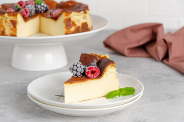 San Sebastian cheesecake with berries and mint leaves on top on a white plate on a gray concrete background. Traditional Spanish dessert. Copy space