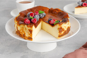 San Sebastian cheesecake with berries and mint leaves on top on a white plate on a gray concrete background. Traditional Spanish dessert. Copy space
