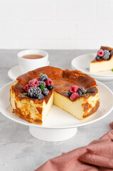 San Sebastian cheesecake with berries and mint leaves on top on a white plate on a gray concrete background. Traditional Spanish dessert. Copy space