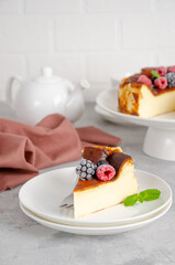 San Sebastian cheesecake with berries and mint leaves on top on a white plate on a gray concrete background. Traditional Spanish dessert. Copy space