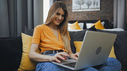 happy freelancer using laptop while sitting on sofa in hotel room
