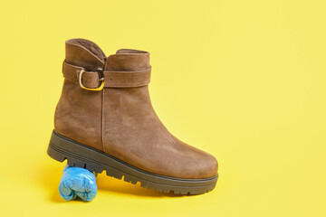 brown suede winter boots and a package of blue plastic shoe covers on a yellow background