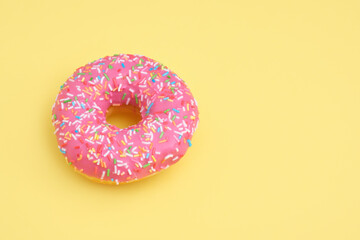 Fototapeta na wymiar Donut with pink icing and pastry sprinkles on yellow background