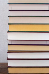 A vertical of stack of books on a wooden shelf and a gray background