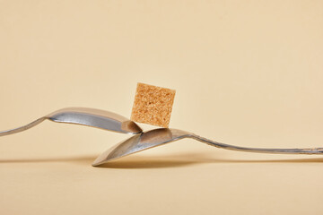 metal spoon with brown sugar cube on beige background, health care and diabetes concept