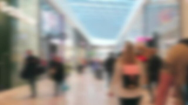 Abstract blurred people customers walking through the interior of modern shopping mall center between shops.