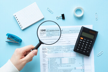 Magnifier zooms in 1040 Individual Income Tax Return. Hand holds a magnifying glass. 1040 tax form 