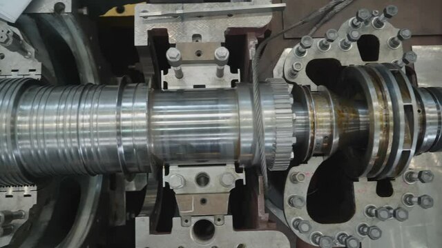 Turbine manufacturing factory. The disassembled turbine is being shown lengthwise with wire laying across it. Heavy Machinery. Many various light gray bolts. Rotary mechanical device. 