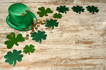 St. Patrick's concept. Green hat, shamrocks and lucky coins on wood background.