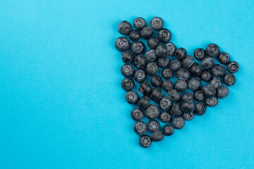 Blueberry in heart shape on bright blue background