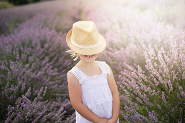 Little toothless girl between lavender plants with straw hat covering her face