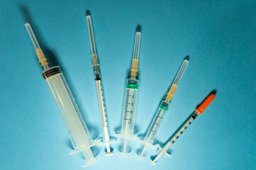 Top view of various types of syringes placed in a semicircle on a blue surface. There are those for vaccines, for insulin, for administering different drugs.
