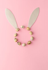 A circle made of quail eggs representing the rabbit's face. The shape of a bunny's ears made of silver foam. Easter pink background concept. Flat lay.
