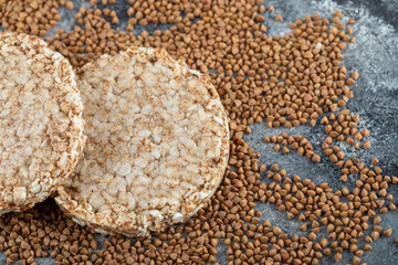 Two crispbread and uncooked buckwheat on marble surface