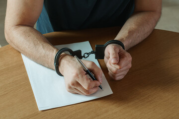 Men hands with handcuffs fill the police record, confession. on top of the police investigative...