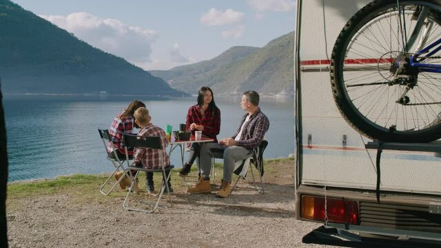 Family eat by rv car Rbbro. Mother and father parents lunch with children kids outdoor on lake. Motorhome travel trip. Concept togetherness, vacation, camper. Campsite breakfast with son and daughter.