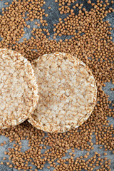 Two rice cakes and uncooked buckwheat on marble surface