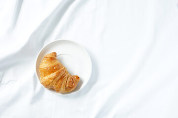 Croissant on white ceramic plate placed on white Crumpled fabric
