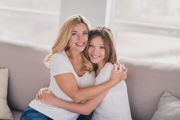 Photo of sweet shiny daughter mom wear white t-shirts smiling hugging sitting sofa indoors inside...