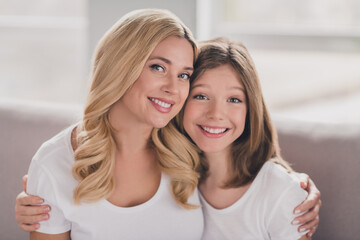 Photo of adorable pretty mommy daughter wear white t-shirts embracing smiling sitting couch inside...