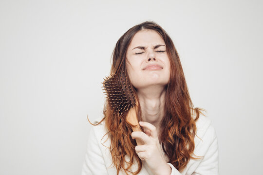 red-haired woman combing tangled curls on a light background