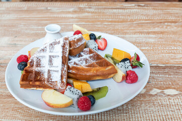 Waffle topped with mixed fruits, syrup, whipped cream, icing sugar and freshly chopped strawberries. Waffles with fresh topicals fruits, stack of waffles with icing sugar.