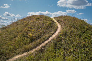 A path among the hills. Summer blue cloudy sky.