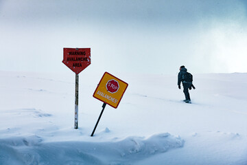 The tourist enters the forbidden dangerous zone of the avalanche in winter time. Warning signs in snow in the foreground. Avalanches danger concept