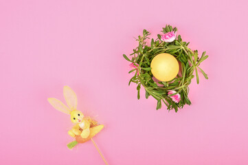 Yellow egg in self-made Easter flower wreath and rabbit toy on pastel backdrop. Easter still life on pink background
