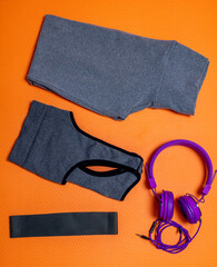 Legging pants with gray top and purple headphones on an orange mat with a black thera band used to exercise at home alone or with friends and family.