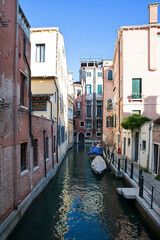 Fototapeta na wymiar Typical narrow street canal in one of the most visited city in the world, with lined up traditional, picturesque houses, with gondolas parking and small access footpath, Venice, Italy