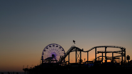 Silhouette of the popular ferris wheel known as the Pacific Wheel and the steel roller coaster known as The Santa Monica West Coaster, on the popular pier at the sunset in Los Angeles, California, USA
