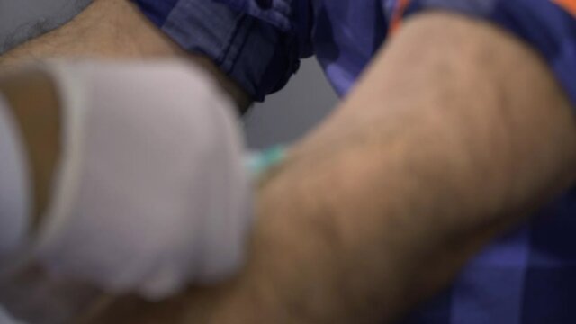 Side close-up, static shot of man arm with a tourniquet while drawing blood with a syringe (needle) a nurse with white gloves.