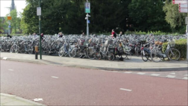 Defocused Bicycle park area next to cycle lanes with people riding past