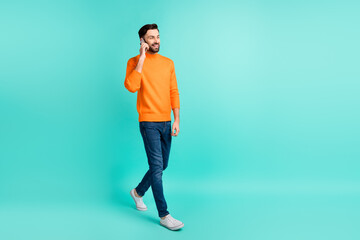 Fototapeta premium Full size profile side photo of young cheerful smiling man go walk talking on phone isolated on turquoise color background