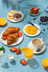 Luxury sunny continental breakfast on blue concrete background table with tropical plants shadows