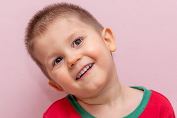 A handsome boy laughs. The boy poses indoors. Pink background