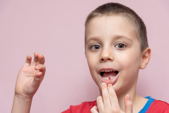 Cute elementary age boy is pulled his baby tooth with hand himself. He is holding the dropped tooth and showing the tooth's place in his mouth. Tooth removal.