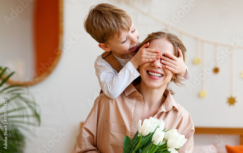 tender son closes his mother's eyes, making her a surprise and gives her a bouquet of tulips, congratulating her on mother's day