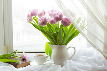 still life a bouquet of lilac tulips in a vase a mug of tea an old book on the window