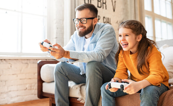 father and daughter laugh and play video games together using a video game console