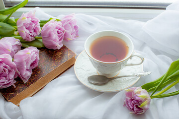 Fototapeta na wymiar mug of tea an old book a bouquet of tulips on the window