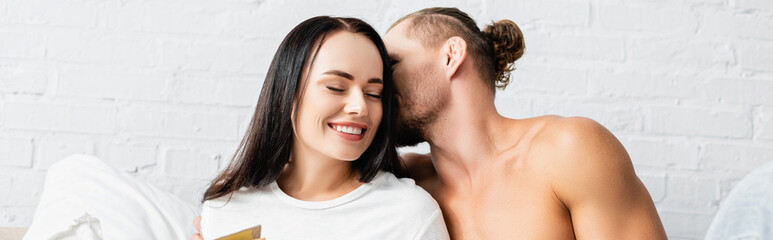 Muscular man kissing smiling woman in bedroom, banner
