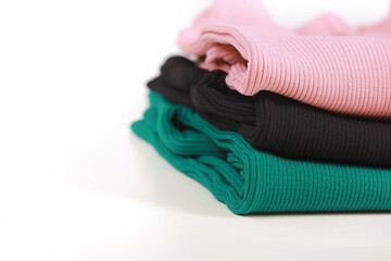 Pile of knitted warm colorfull sweaters with different knitting patterns folded in stack on white background, white wall background. Fall winter season knitwear. Close up, copy space for text